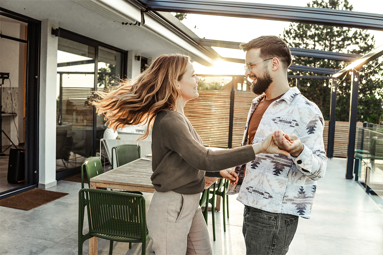 Een gelukkige man en vrouw dansen samen op een terras tijdens zonsondergang.