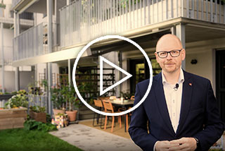 Mann im Anzug steht vor einem modernen Gebäude mit Terrassensituation und outdoor Möbeln, Spiel mit Licht und Schatten.