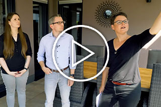 Drie mensen in een terrassituatie, één persoon wijst met de hand en de anderen kijken toe.