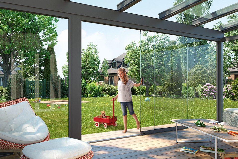 Een moderne terrasoverkapping met glazen wanden en een meisje met een speelgoedauto in de tuin. Een moderne terrasoverkapping met glazen wanden en een meisje met een speelgoedauto in de tuin.