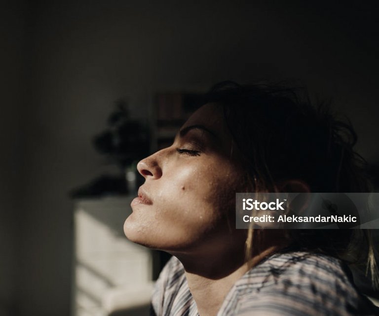 Frau mit geschlossenen Augen, die das Licht genießt, im Hintergrund eine dunkle Silhouette.