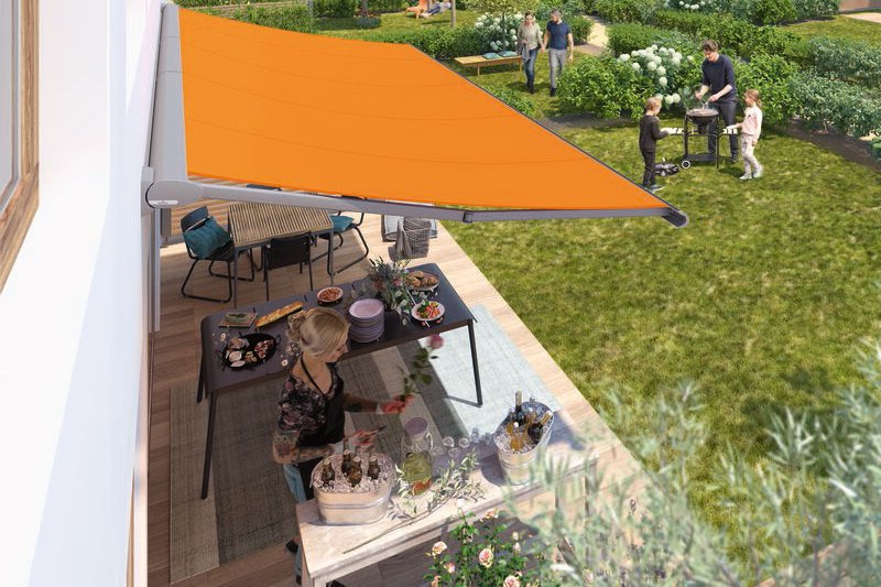Een terrasoverkapping met een oranje zonweringdoek, een tuin met mensen en een tafel vol eten. Een terrasoverkapping met een oranje zonweringdoek, een tuin met mensen en een tafel vol eten.