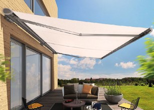 Een witte zonnescherm boven een terras met een zithoek en uitzicht op een groene tuin. 