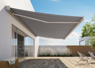Zijde markies uitgerust met een grijs zonweringdoek, over een houten terras met moderne meubels. 