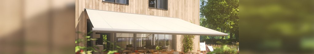 Een huis met een lichte zonnescherm boven een terras, omgeven door groen.