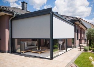 Moderne overkapping met een grijs zonweringdoek en glazen wanden, gelegen aan een huis met een terras. 