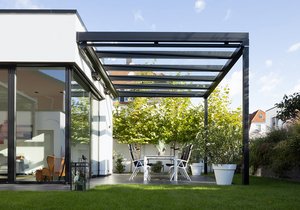 Een moderne overkapping met glazen schuifwanden en een terras met witte meubels en groene planten.