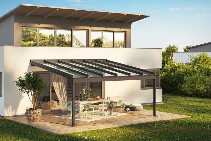 Moderne woning met een overkapping en terras in een groene omgeving onder een blauwe lucht.
