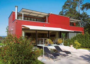 Modern gebouw met rode gevel, overkapping en ligbedden in de tuin. 