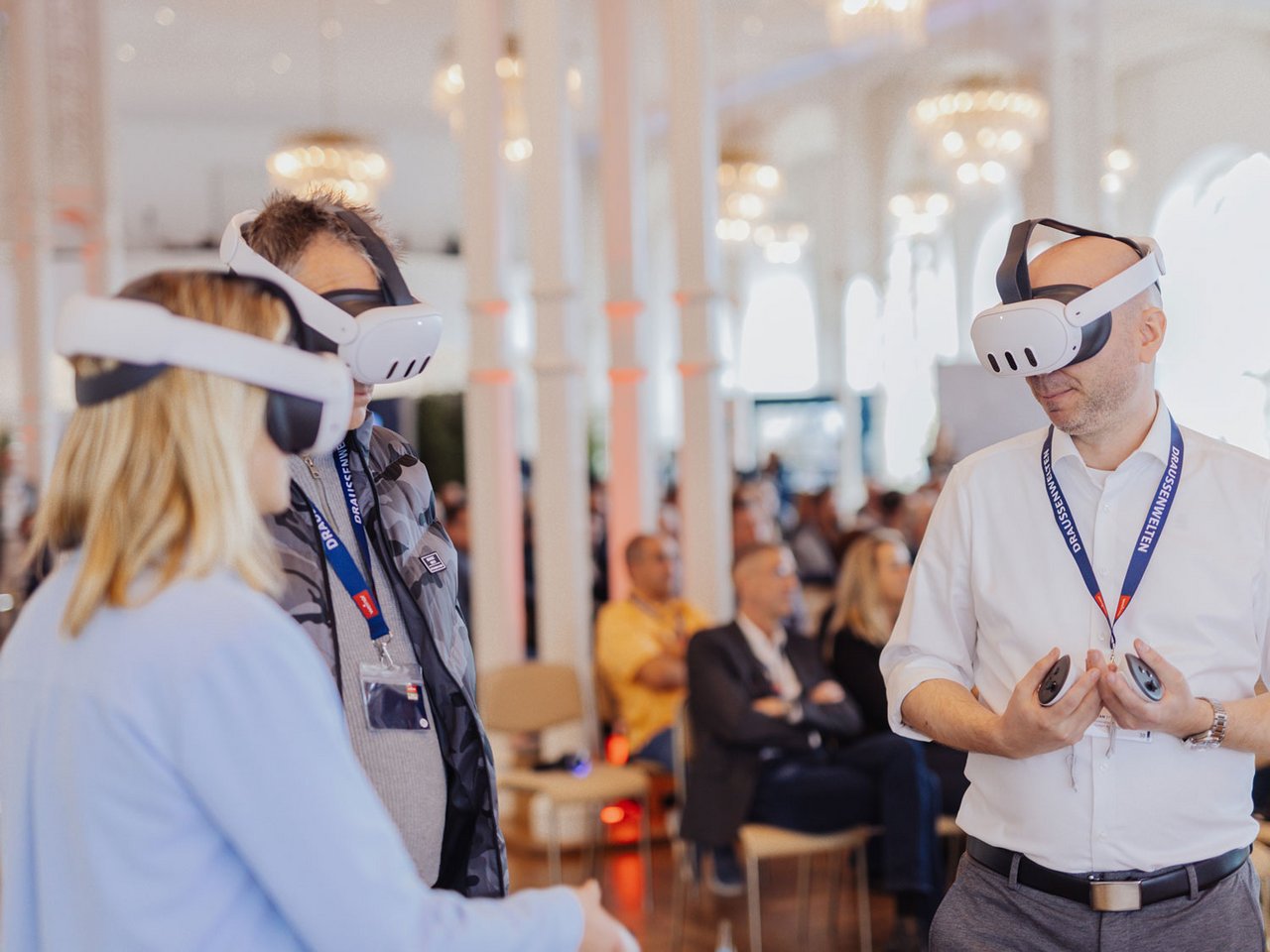 Drie mensen met virtual reality-brillen in een drukke zaal met een lichte, moderne uitstraling.