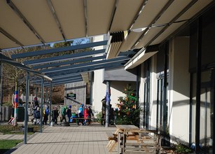 Een overkapping met zonneschermn en kinderen die voorbijlopen, met kerstboom en groene grasvelden. 