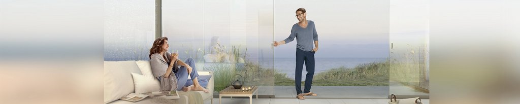 Twee mensen in een moderne omgeving met glazen schuifwanden en uitzicht op zee.