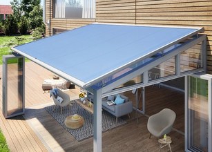 Een moderne overkapping met een blauw zonweringdoek en glazen schuifwanden, gelegen op een houten terras. 