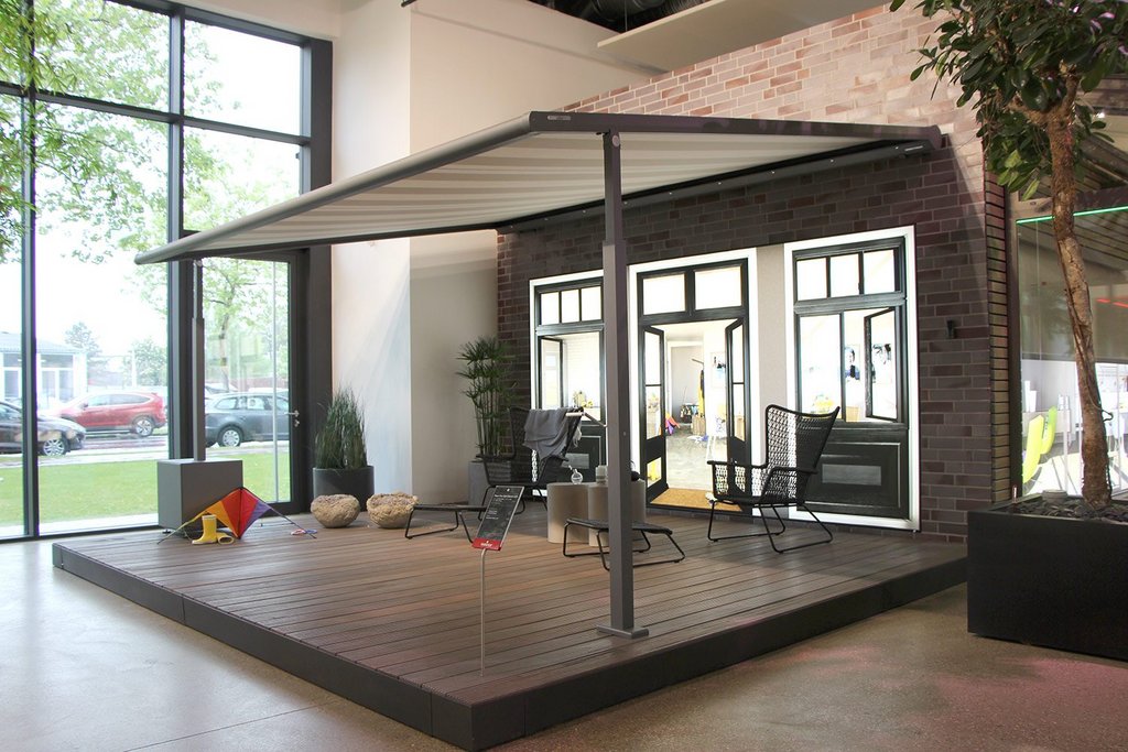 Terrassensituatie met een overkapping, glazen wanden en verschillende meubels in een moderne omgeving.