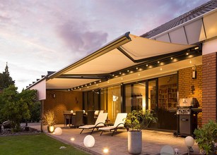 Terrassensituatie met een zonnescherm, verlichting en meubels onder een avondlucht. 