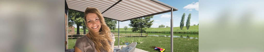 Een vrouw lacht onder een overkapping met een grijs zonweringdoek, omringd door groen landschap. Een vrouw lacht onder een overkapping met een grijs zonweringdoek, omringd door groen landschap.