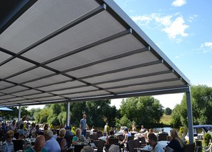 Terrasoverkapping met een rechtlijnig ontwerp en een grijs zonweringdoek, met uitzicht op een drukke buitenruimte. 